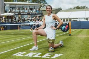 Rebecca Marino kneels on the grass court at Ilkley behind the trophy. She plays this week in qualifying at Wimbledon.