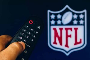 In this photo illustration a close-up of a hand holding a TV remote control seen displayed in front of the NFL Network logo